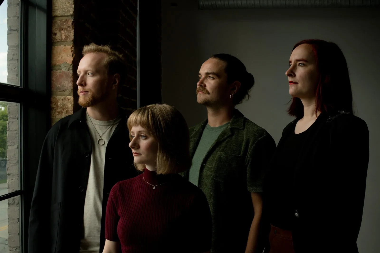 The four members of Anchorites standing together, lit warmly against a brick and window interior